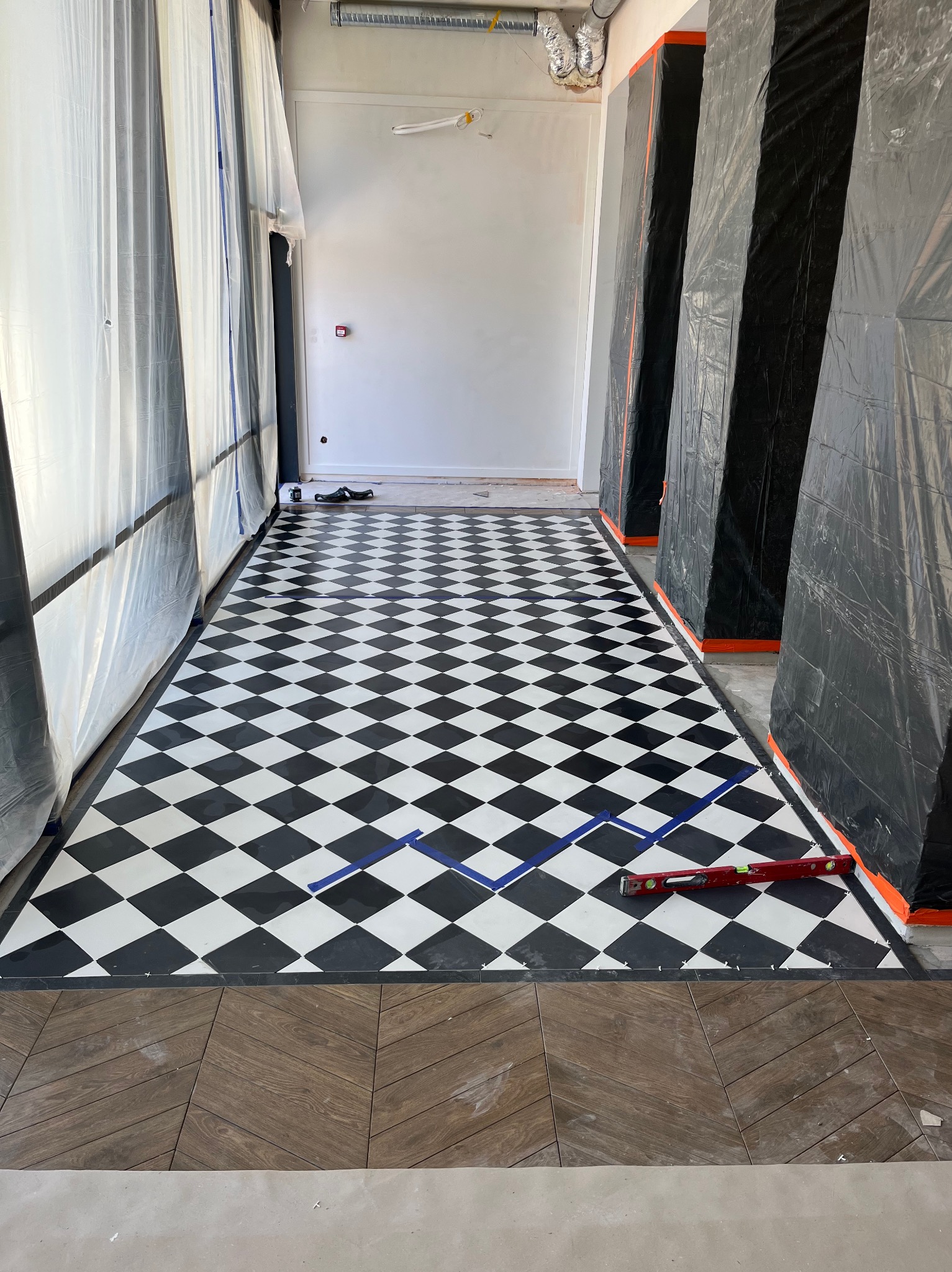 Ułożona podłoga w czarno-białą szachownicę, z poziomnicą i taśmą malarską, zabezpieczone ściany folią malarską. Fragment parkietu w jodełkę.