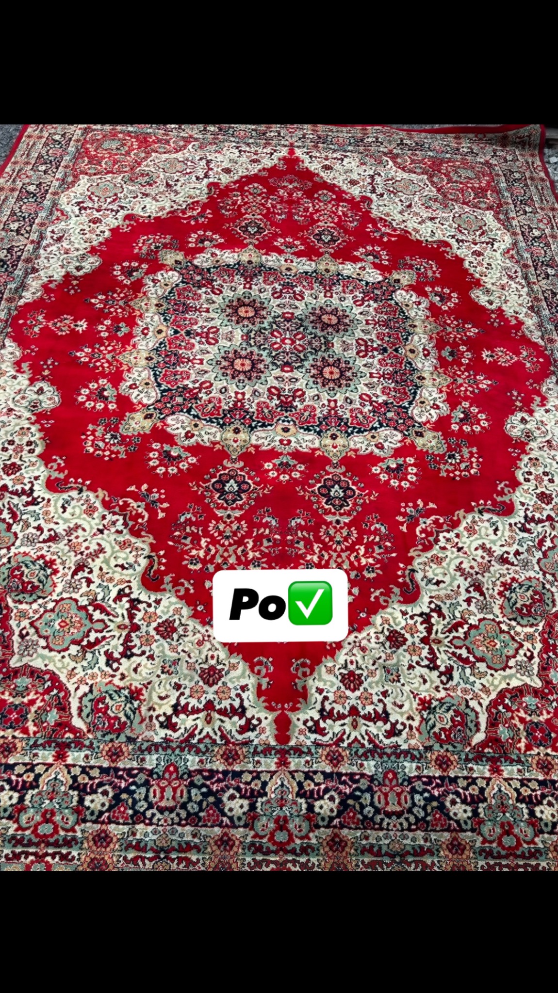 Czerwony dywan z bogatym, symetrycznym wzorem orientalnym, sfotografowany z góry. Na dywanie widoczny znak 'PoV' z zielonym symbolem akceptacji.