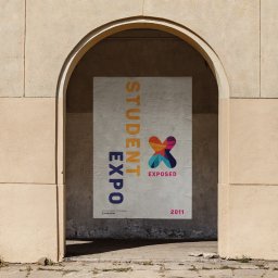 Katarzyna Rębacz - Plakat 'Student Expo' z kolorowym logo w kształcie X, umieszczony w arkadzie budynku. Tekst pionowo po lewej, rok 2011 w prawym dolnym rogu. Stonowana kolorystyka.