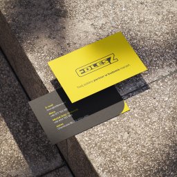 Katarzyna Rębacz - Dwie wizytówki firmy budowlanej EDLESZ leżące na betonowych schodach w ostrym świetle słonecznym. Jedna żółta z logo, druga szara z danymi kontaktowymi.