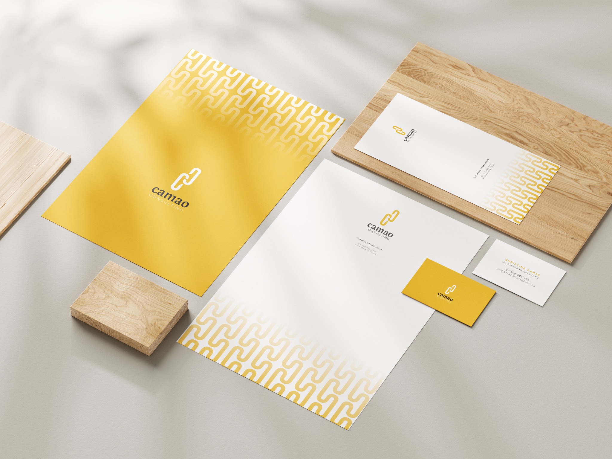 Komplet materiałów firmowych z żółtym motywem: wizytówki, papier firmowy i teczka, ułożone na drewnianych podstawkach w minimalistycznej aranżacji.