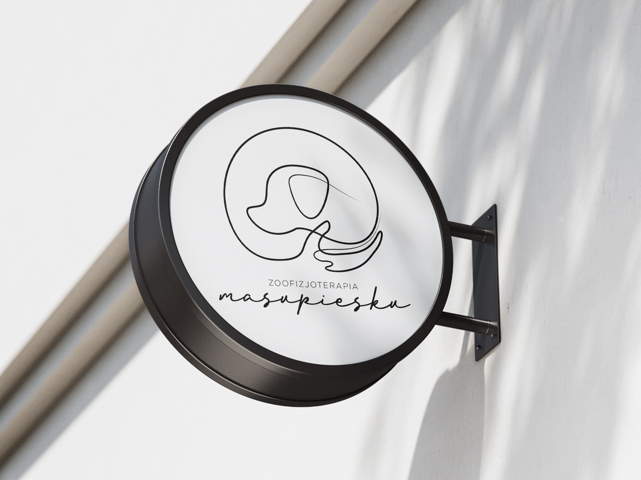 Okrągły szyld z minimalistycznym logo przedstawiającym psa i napisem 'zoofizjoterapia masupiesku', zamontowany na białej ścianie w cieniu.