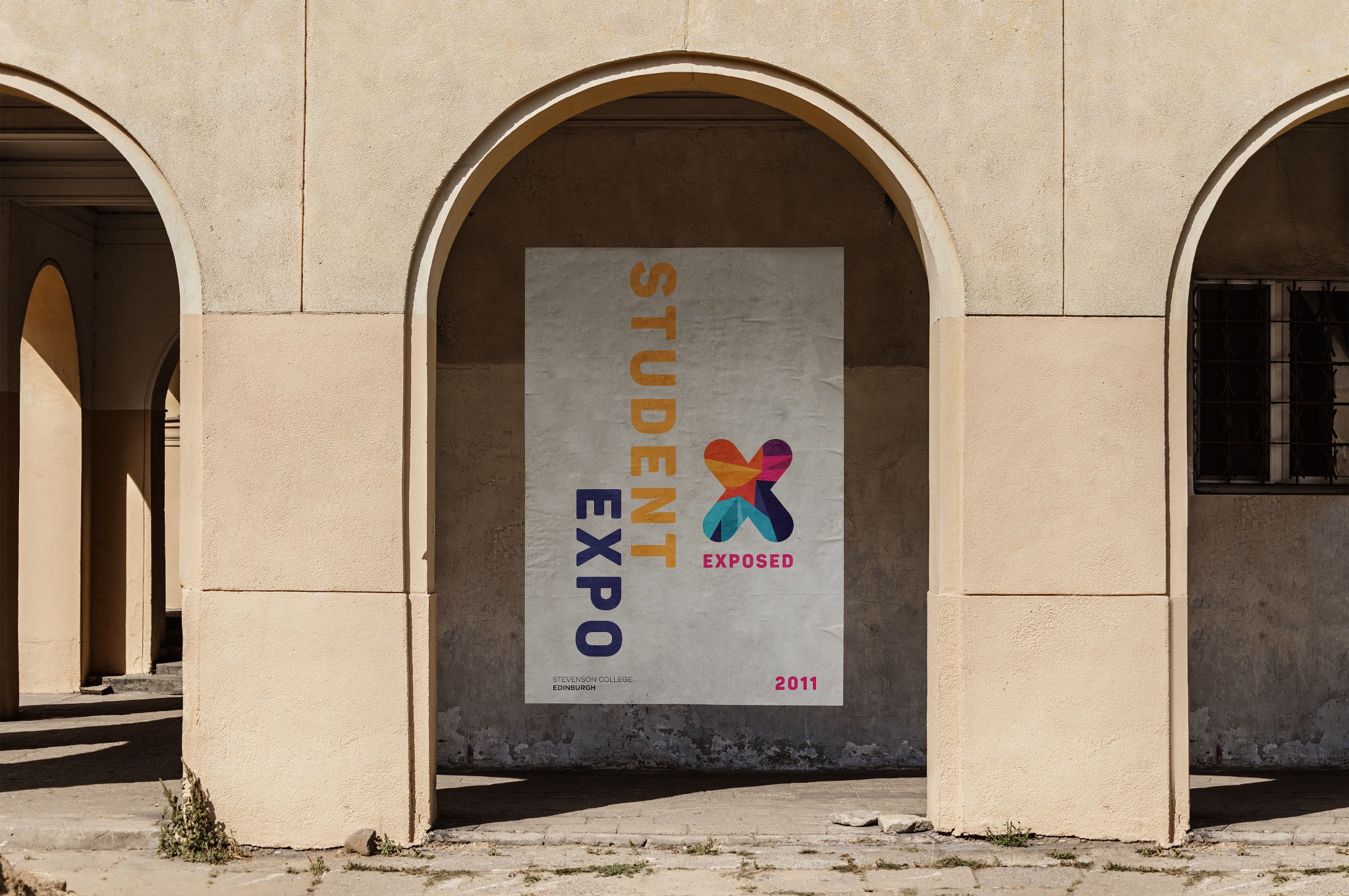 Plakat 'Student Expo' z kolorowym logo w kształcie X, umieszczony w arkadzie budynku. Tekst pionowo po lewej, rok 2011 w prawym dolnym rogu. Stonowana kolorystyka.
