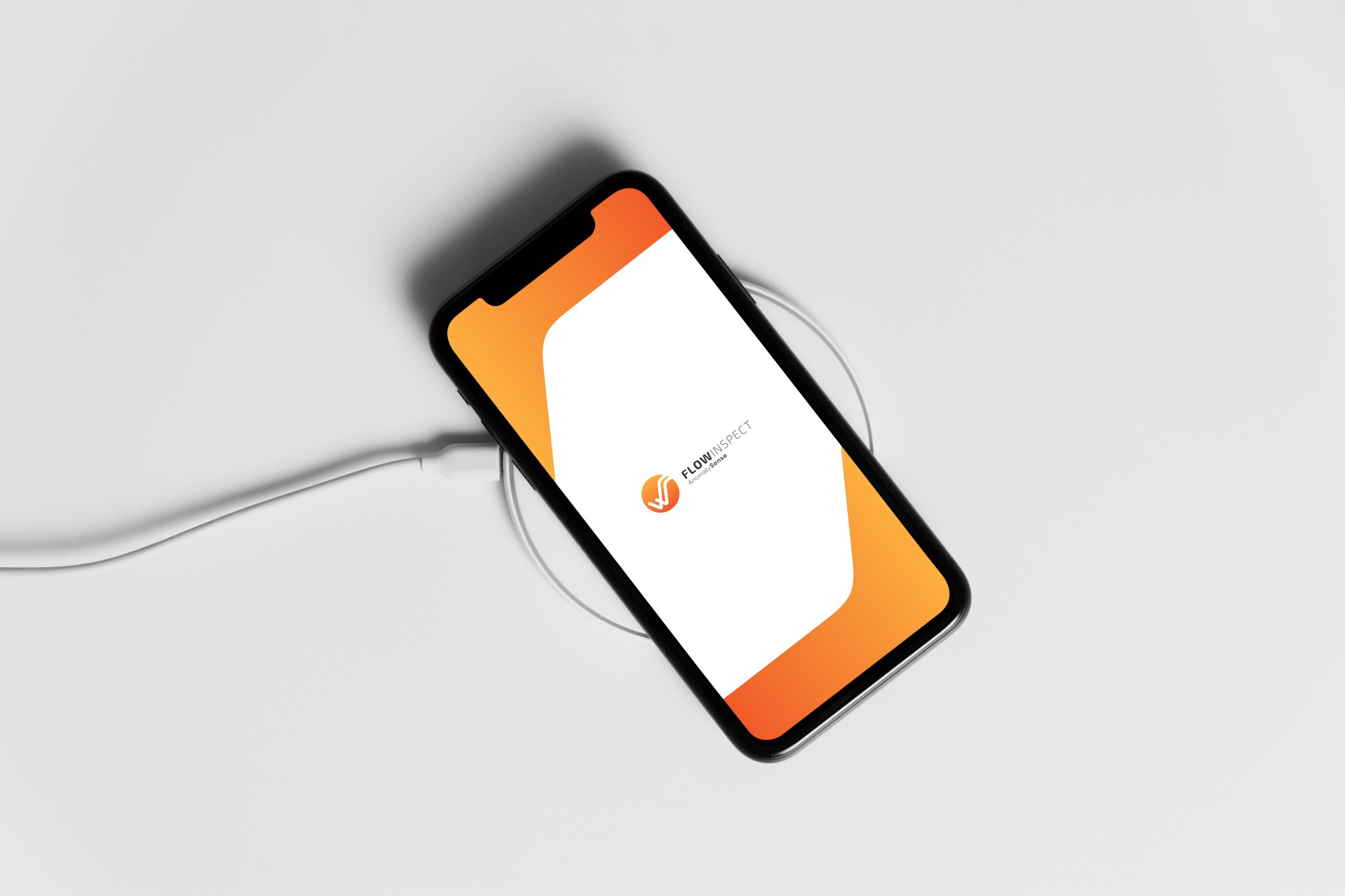 Smartfon z logo FlowInspect na ekranie, leżący na białym tle i podłączony do ładowarki. Minimalistyczny design z pomarańczowymi akcentami.
