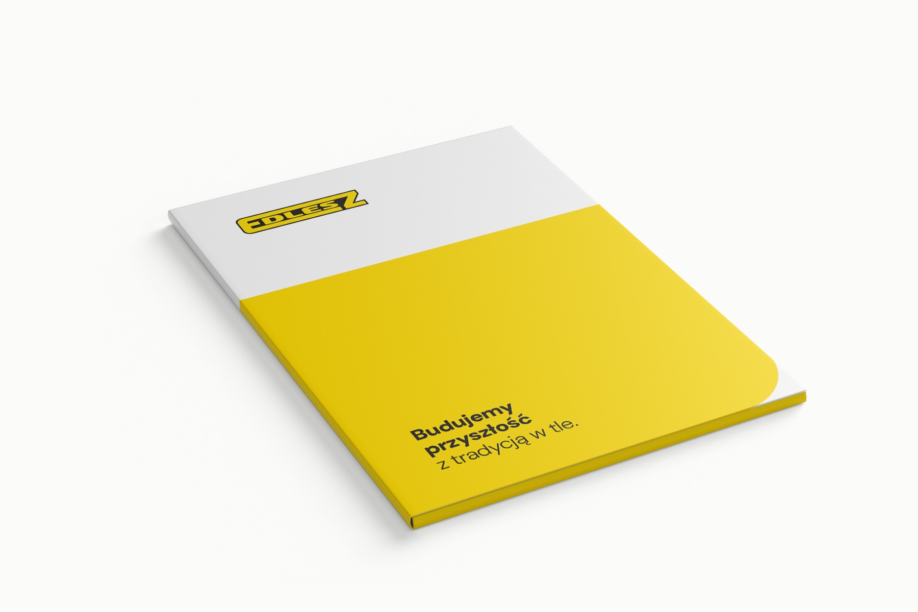 Biało-żółta broszura z logo i hasłem 'Budujemy przyszłość z tradycją w tle' leżąca na białym tle, prezentowana pod kątem.