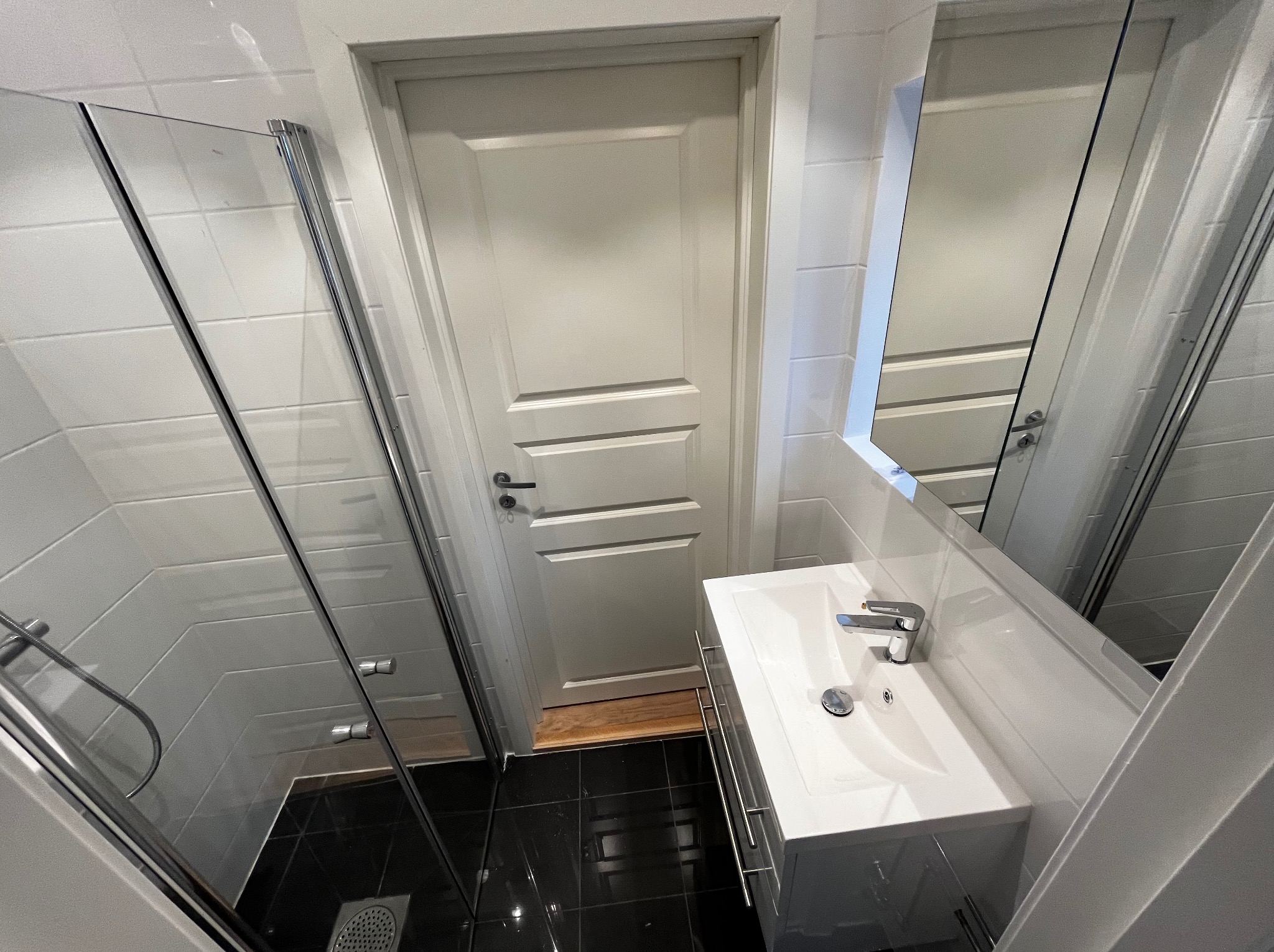 Nowoczesna łazienka z kabiną prysznicową, białą umywalką z szafką i czarną podłogą. Widok z góry, ukazujący minimalistyczny design i funkcjonalne rozwiązania.