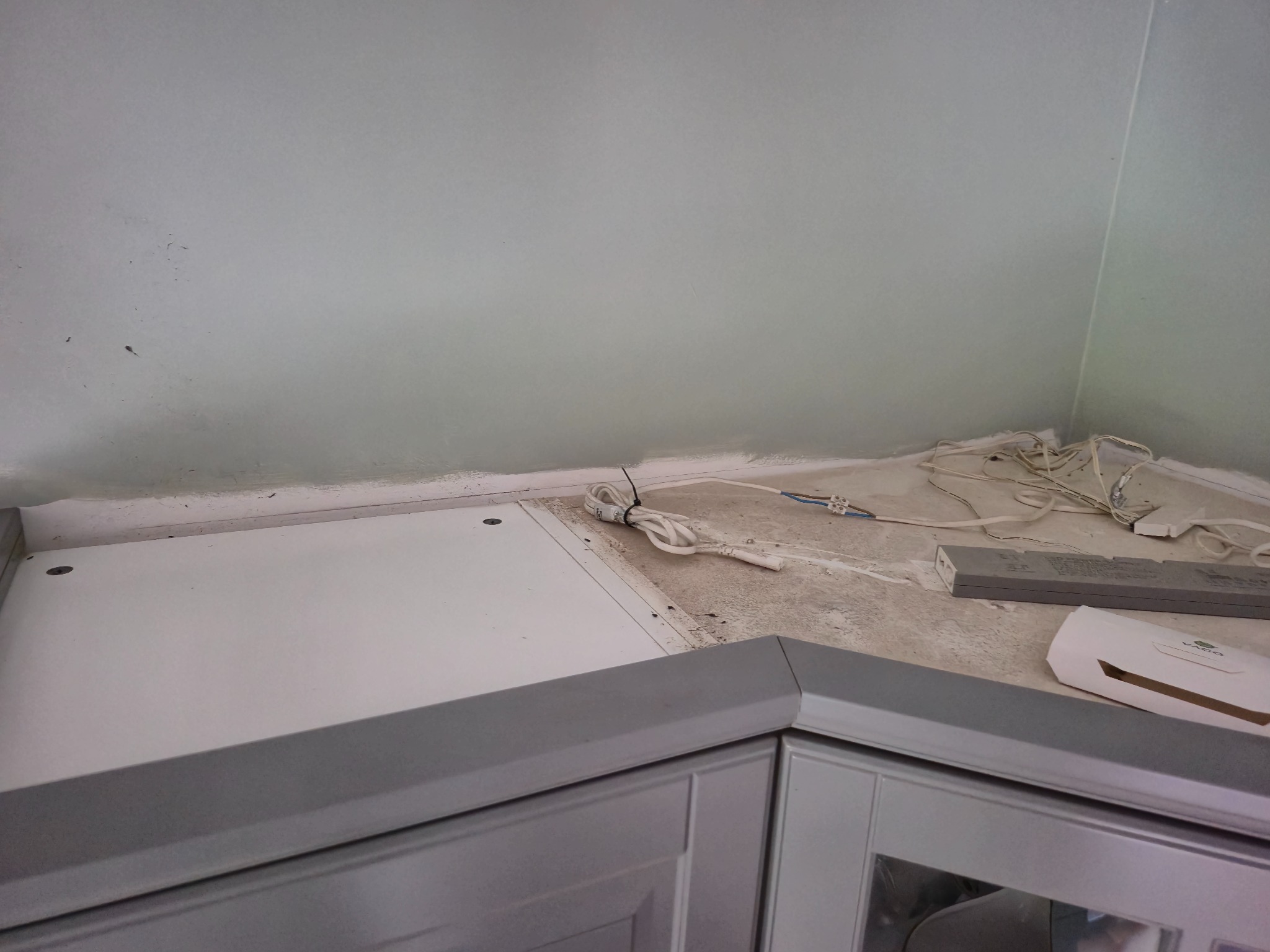 Niedokończony montaż blatu kuchennego z widocznymi kablami i elementami oświetlenia LED. Ściana wymaga wykończenia, widoczne ślady po pracach remontowych.