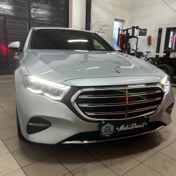 Mateusz Jankowski - Błyszczący, srebrny Mercedes po detailingu, z widocznym logo firmy na tablicy rejestracyjnej, na tle garażu z wyposażeniem do ćwiczeń.