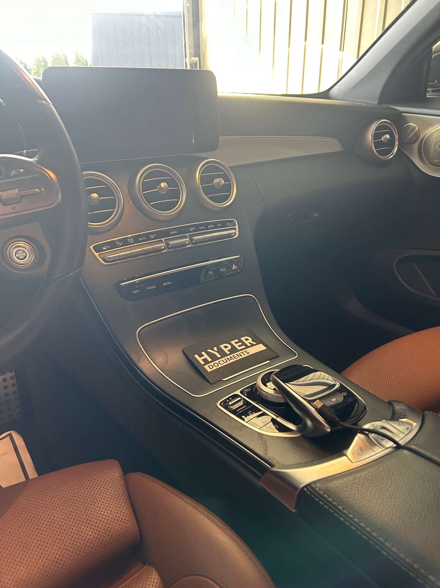 Wnętrze luksusowego samochodu z brązową skórzaną tapicerką, widok na deskę rozdzielczą i konsolę środkową. Widoczne detale wykończenia i elementy sterowania.