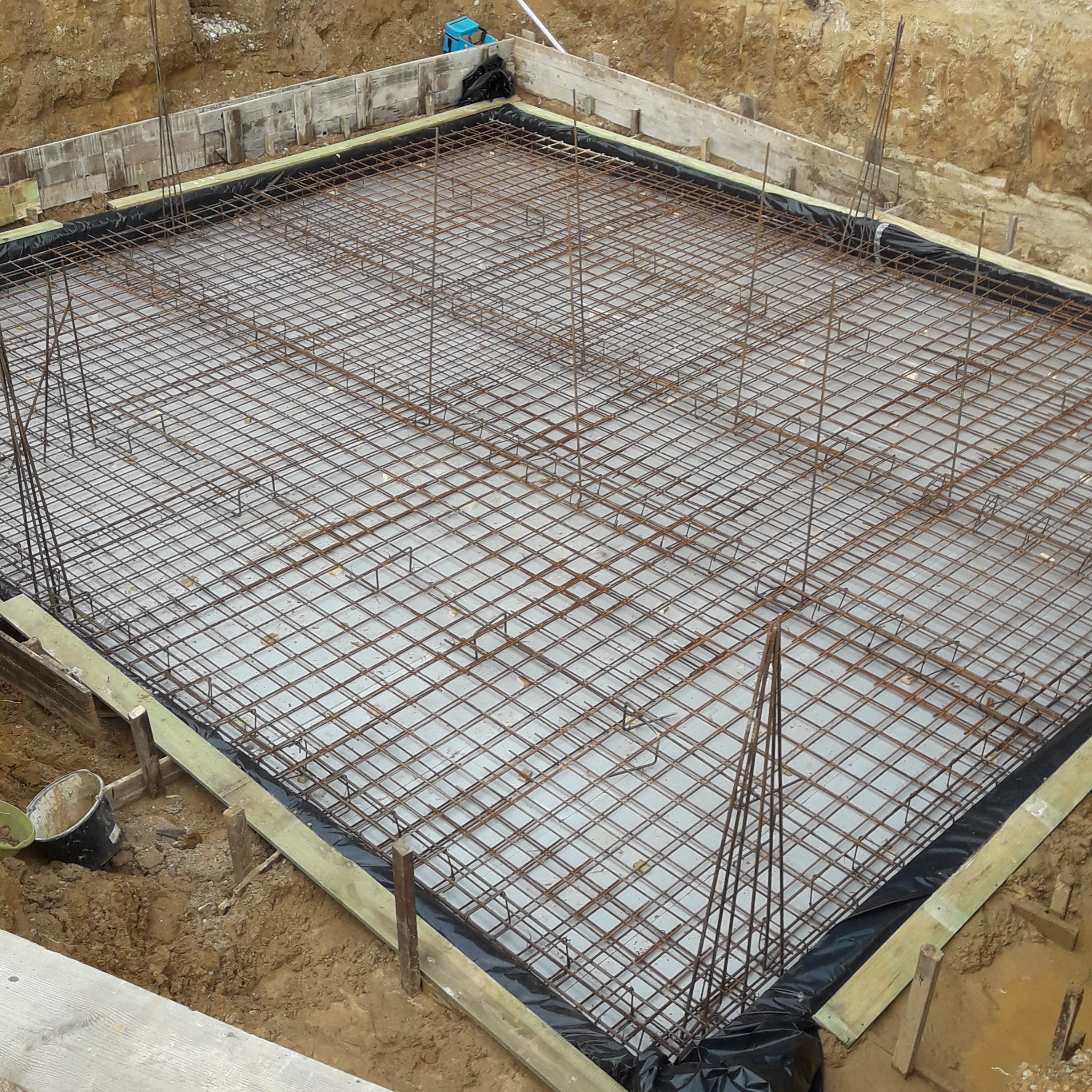 Zbrojenie fundamentu domu jednorodzinnego, widok z góry. Siatka z prętów stalowych na folii, szalunek z desek. Przygotowanie do wylania płyty fundamentowej.