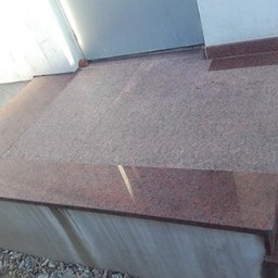 Kamieniarstwo RADEK - Granitowe schody zewnętrzne z czerwonego kamienia, prowadzące do drzwi. Widoczne detale wykończenia i faktura kamienia. Ujęcie z dołu, podkreślające solidność.