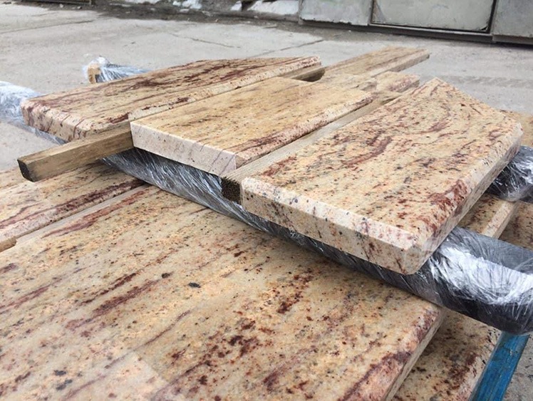 Gotowe elementy z piaskowanego kamienia o ciepłej barwie, zabezpieczone folią i drewnianymi przekładkami, czekają na montaż. Widoczne detale wzoru kamienia.