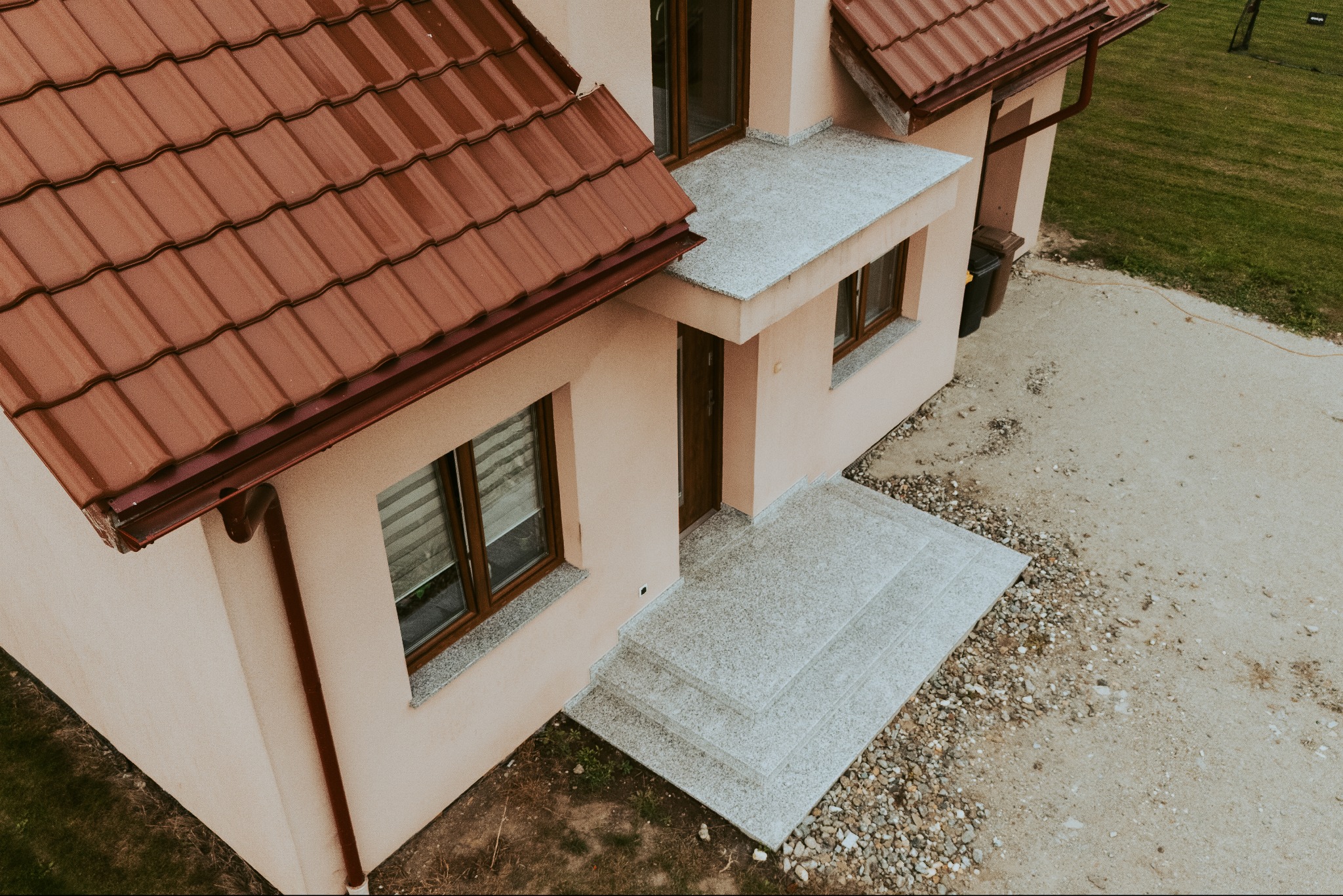 Zewnętrzne schody kamienne prowadzące do domu z beżową elewacją i brązowym dachem, widok z góry. Szare stopnie z kamienia naturalnego.