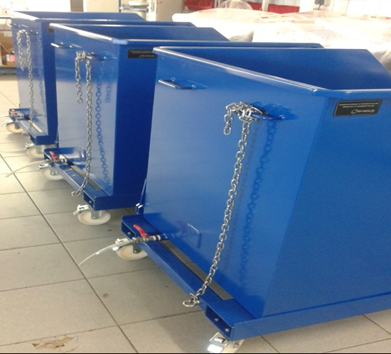 Rząd niebieskich, metalowych pojemników na kółkach z łańcuchami, ustawionych na kafelkach. Widoczne zawory i tabliczki z nazwą producenta.