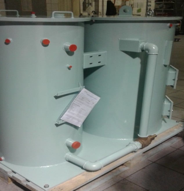 Dwa cylindryczne zbiorniki przemysłowe w odcieniach szarości, połączone rurami. Widoczne detale spawania i dokumentacja techniczna na jednym ze zbiorników.