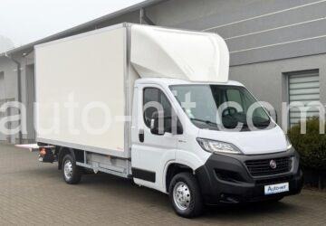 Biały furgon dostawczy z nadbudową, zaparkowany w Warszawie, widoczny z boku na tle szarego budynku. Lekko pochmurna pogoda.