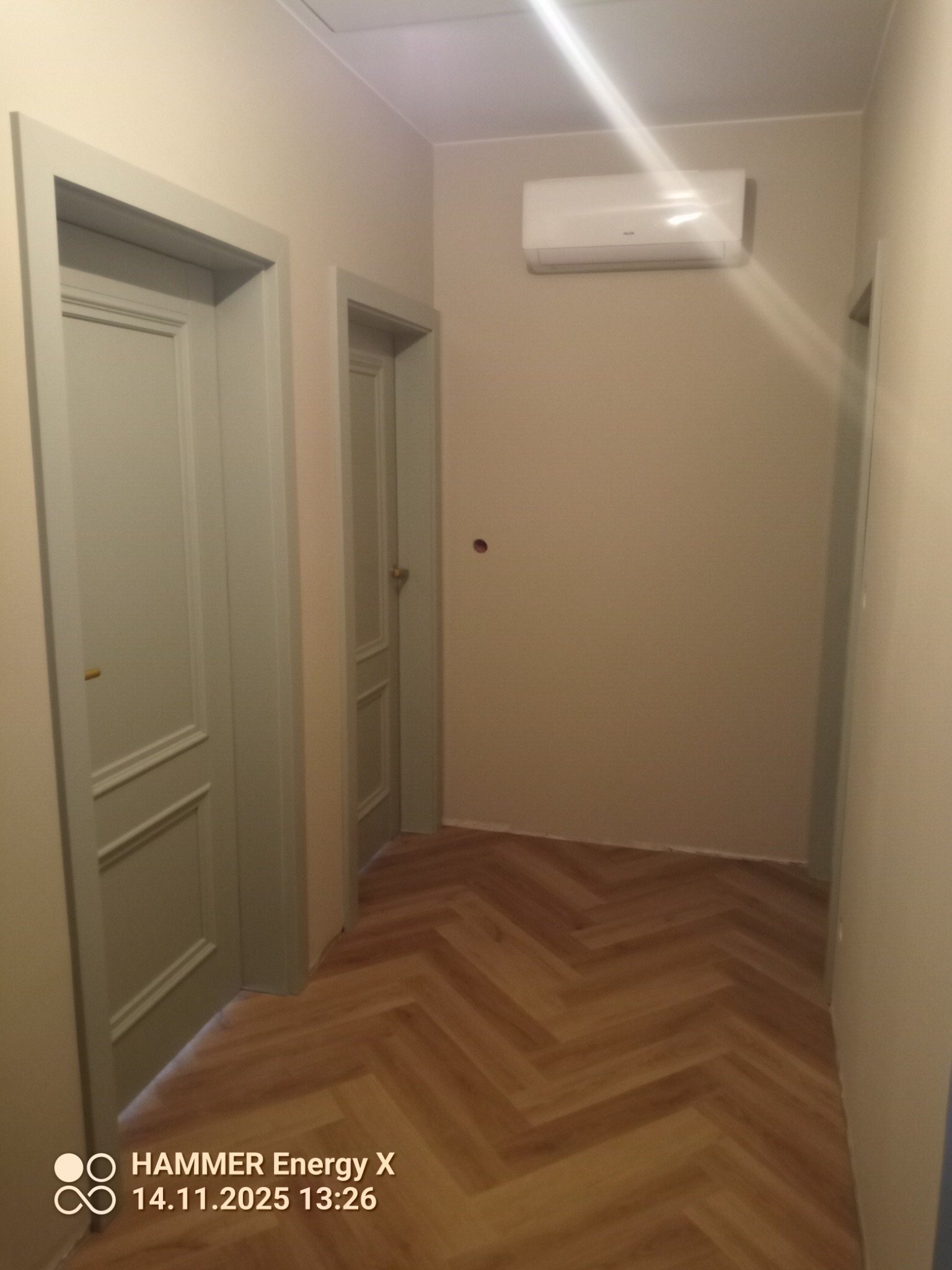 Korytarz po remoncie: dwie szare, panelowe drzwi, parkiet ułożony w jodełkę, klimatyzator na ścianie. Widok na odnowione wnętrze z perspektywy podłogi.