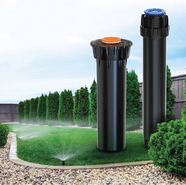 Dwa czarne zraszacze ogrodowe na trawniku, z widocznymi strumieniami wody, na tle żywopłotu i błękitnego nieba. System nawadniania w akcji.