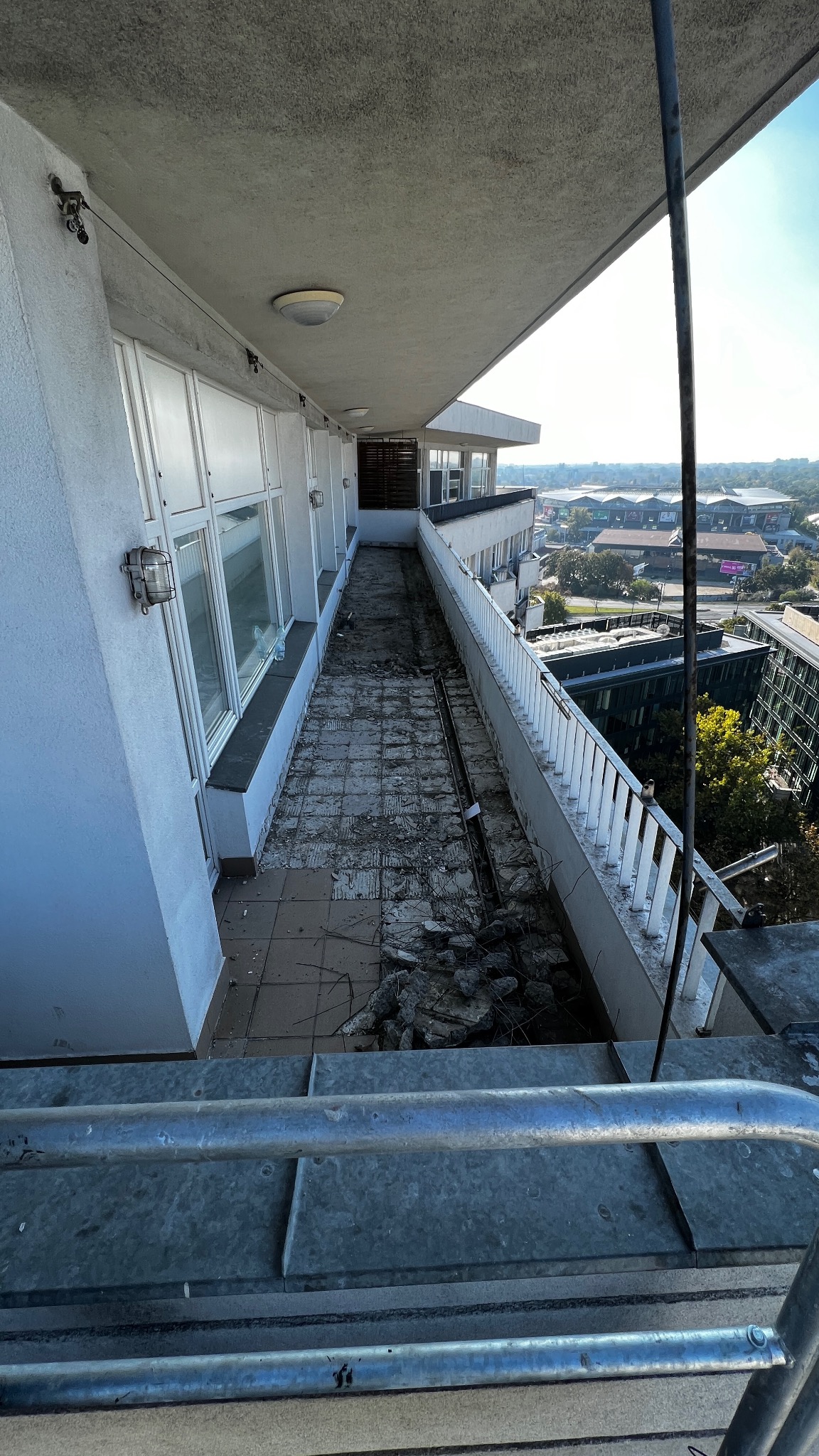 Zdemontowane płytki na balkonie budynku wielopiętrowego, widok z góry na gruz i odsłoniętą konstrukcję. Prace remontowe w toku, widoczne elementy zabezpieczeń.