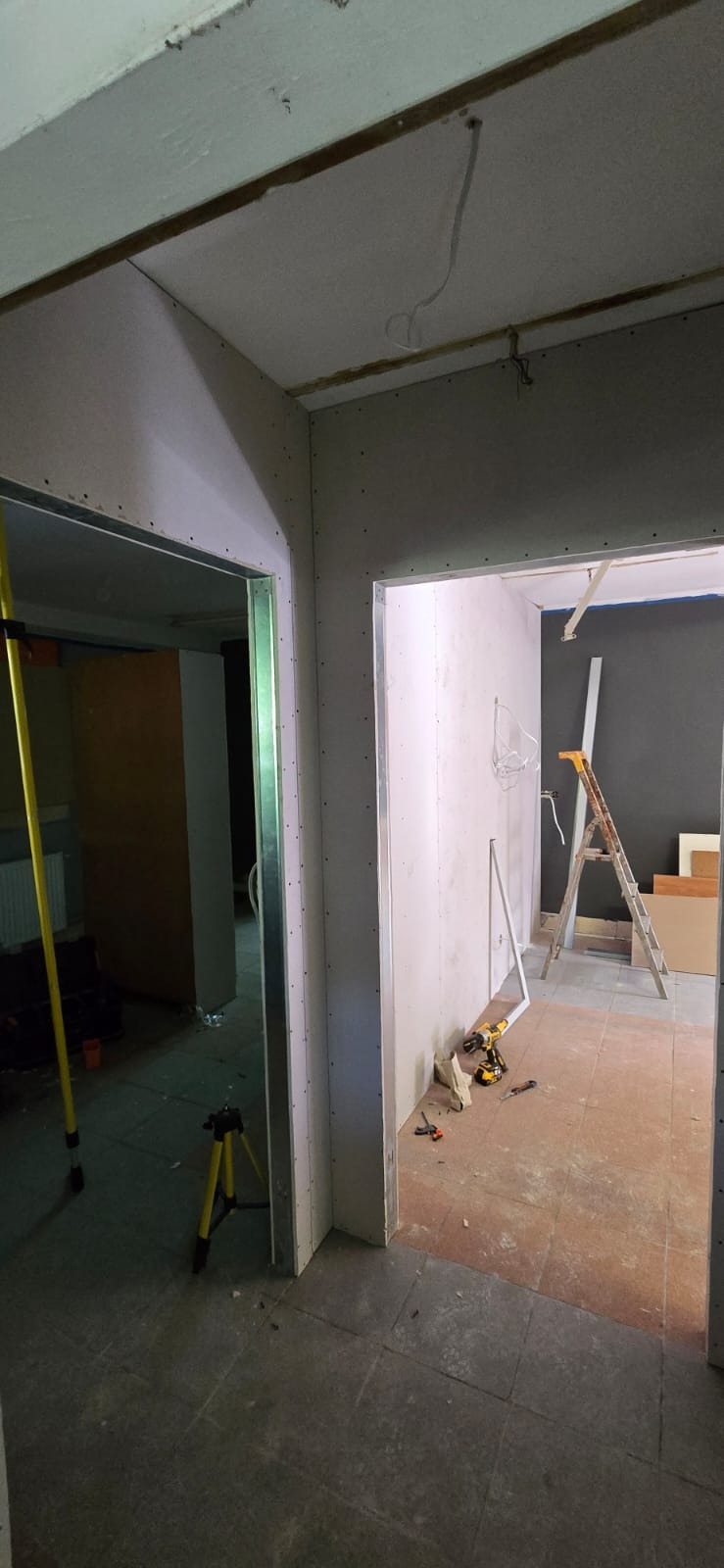 Montaż płyt karton-gips na metalowym stelażu w trakcie prac wykończeniowych. Widoczne narzędzia, drabina i elementy konstrukcyjne ścian działowych.