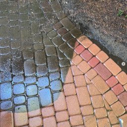 Mazo Wash Krystian Balcerzak - Częściowo umyta kostka brukowa w odcieniach czerwieni i brązu, widoczna różnica w czystości między umytą a zabrudzoną powierzchnią.