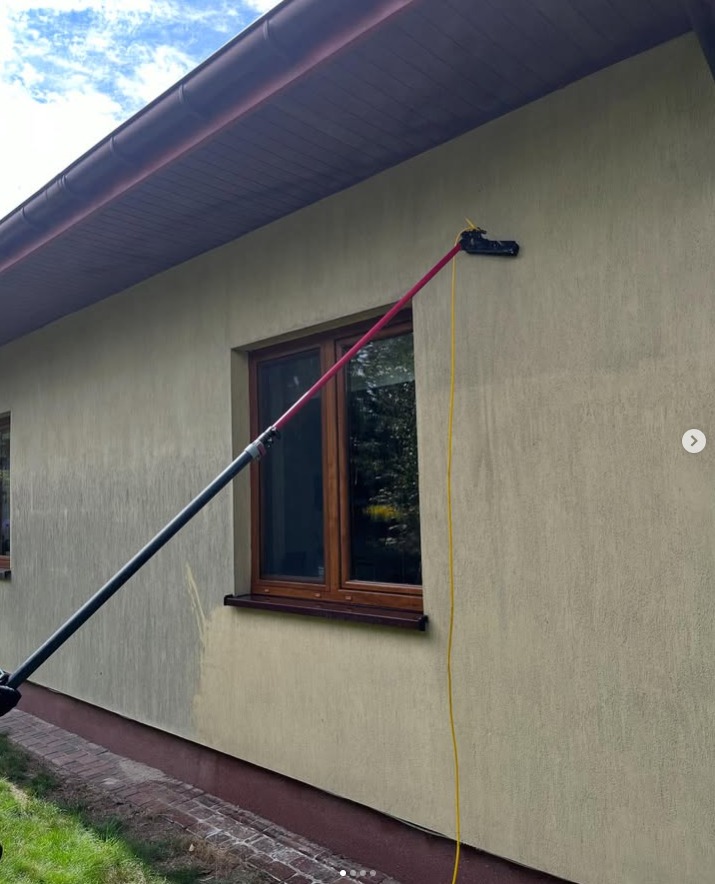 Elewacja domu czyszczona lancą teleskopową. Widoczny fragment ściany przed i po zabiegu. Okno z brązową ramą. Żółty przewód. Częściowo widoczny dach.
