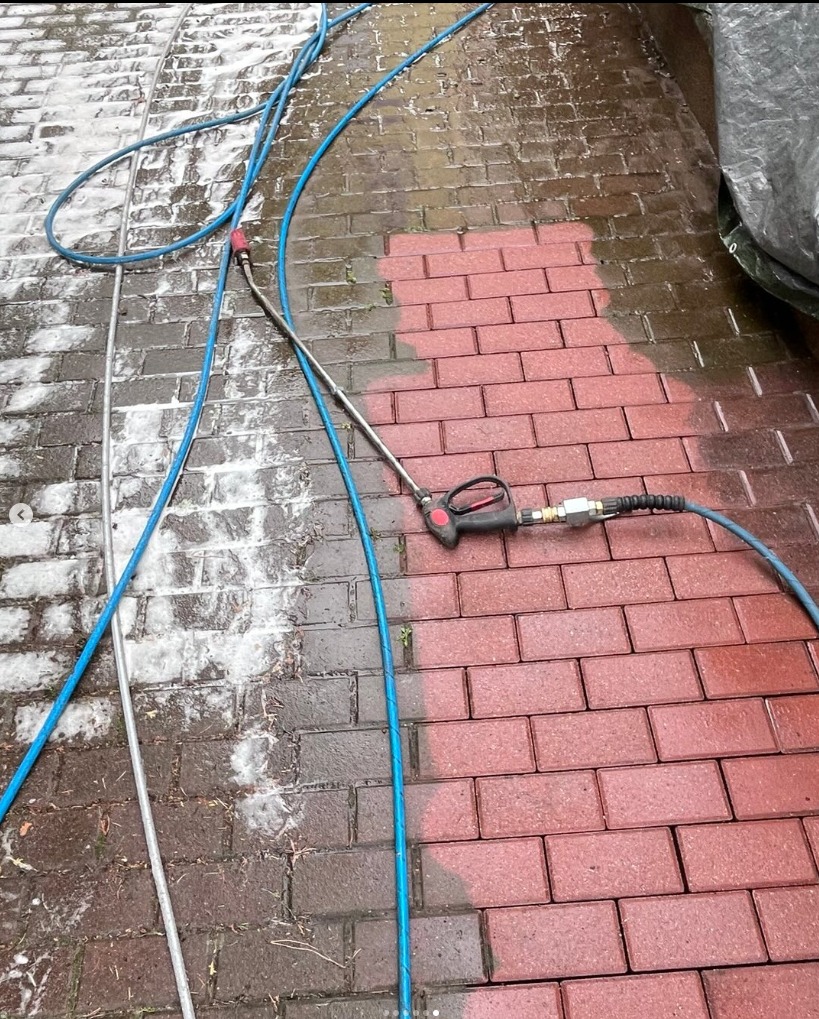 Mycie kostki brukowej: efekt przed i po z użyciem myjki ciśnieniowej. Połowa kostki czysta, czerwona, druga połowa brudna, szara. Widoczny wąż i lanca myjki.