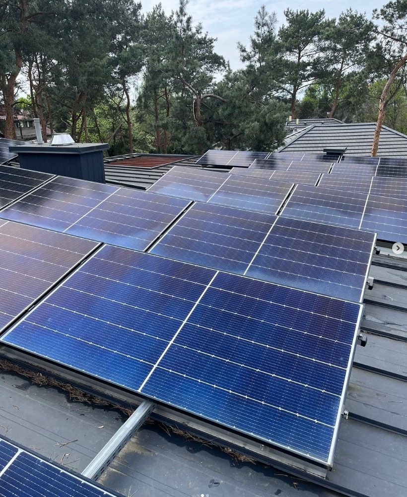 Panele słoneczne na dachu domu, widok z góry, z zanieczyszczeniami między panelami, drzewa w tle.