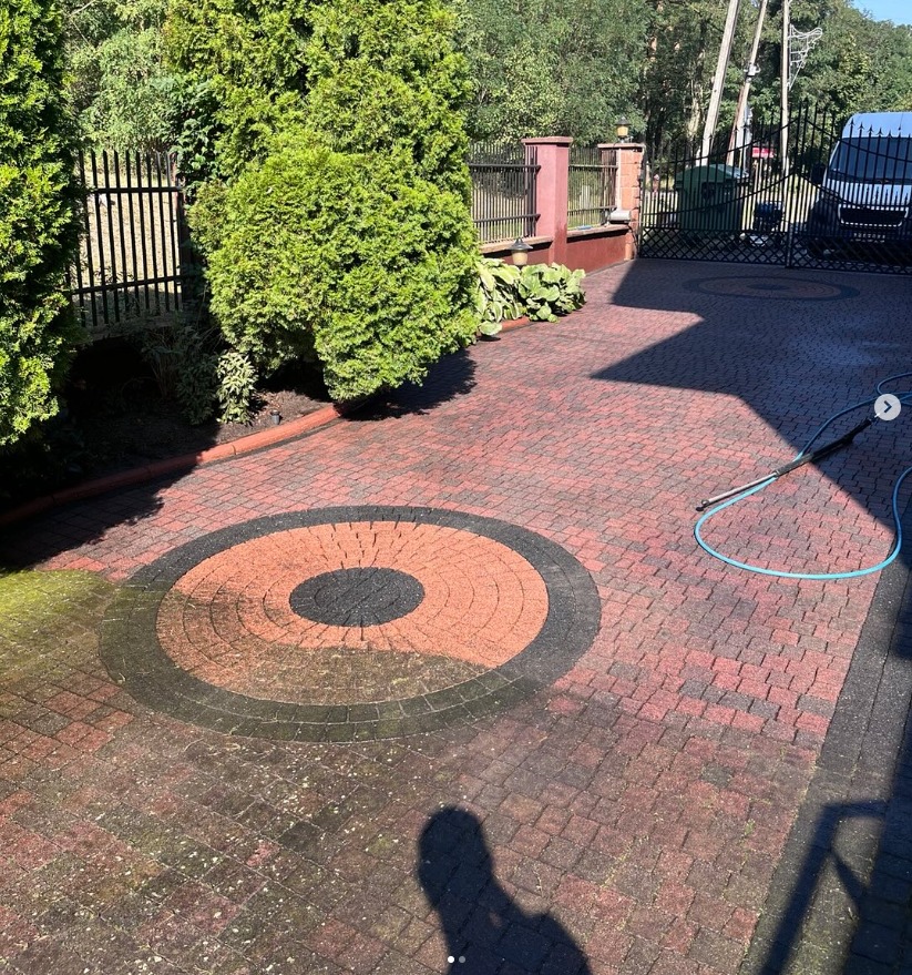 Czyszczenie kostki brukowej z wzorem koła, widoczna różnica przed i po myciu. Część kostki jest jeszcze brudna, a część już umyta. Wąż ciśnieniowy leży na kostce.