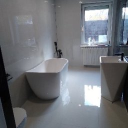 Remonty Bydgoszcz - Nowoczesna łazienka z wolnostojącą wanną o obłych kształtach, białą umywalką na postumencie i błyszczącymi, jasnymi płytkami. Minimalistyczny design, widok z perspektywy podłogi.