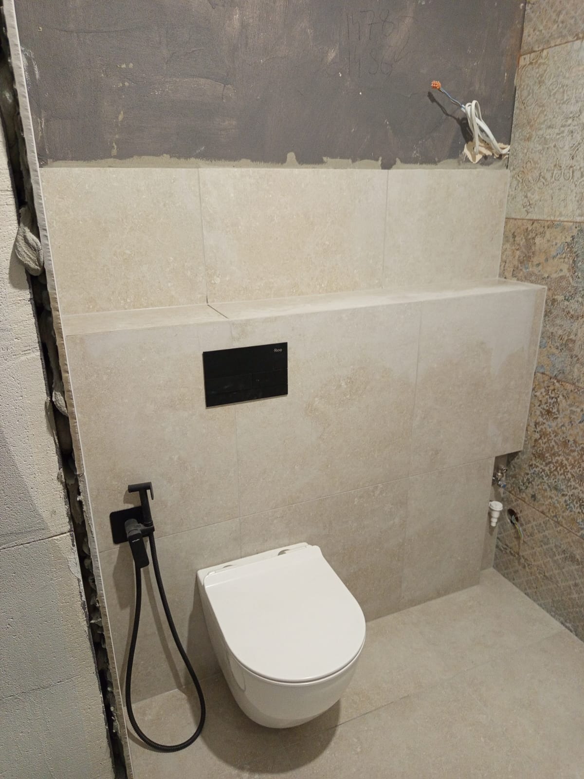 Podtynkowa toaleta z bidetką w jasnej łazience w Bydgoszczy. Częściowo wykończone ściany z beżowych płytek, widoczne instalacje. Minimalistyczny design.