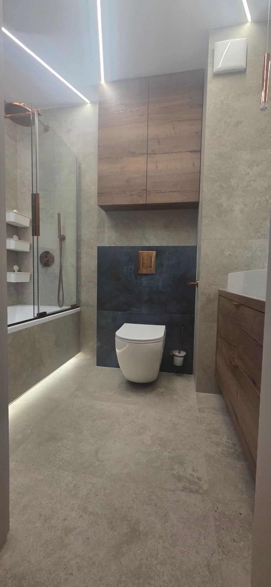 Nowoczesna łazienka z podświetleniem LED: wanna z parawanem, podwieszana toaleta, szafki z drewnianym fornirem i szara płytka imitująca kamień.