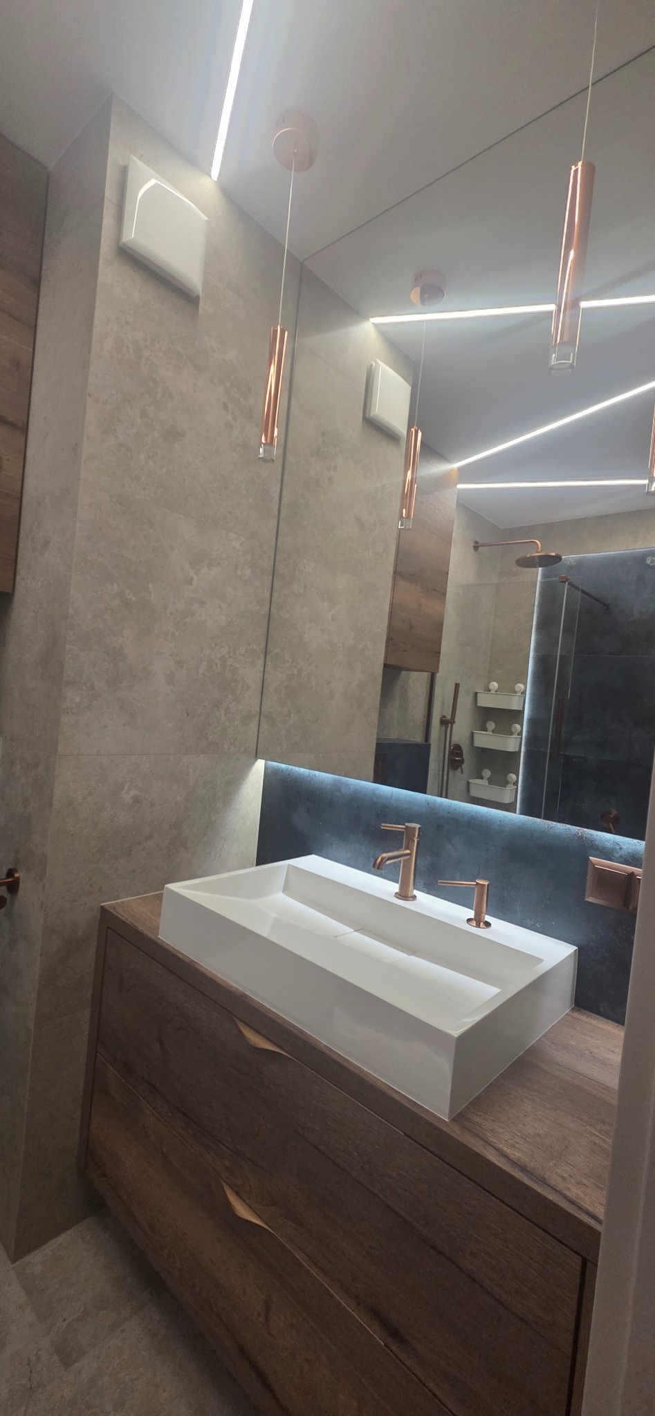 Nowoczesna łazienka z drewnianą szafką pod umywalką, białą umywalką i miedzianą armaturą. Oświetlenie LED i lustro dodają elegancji.