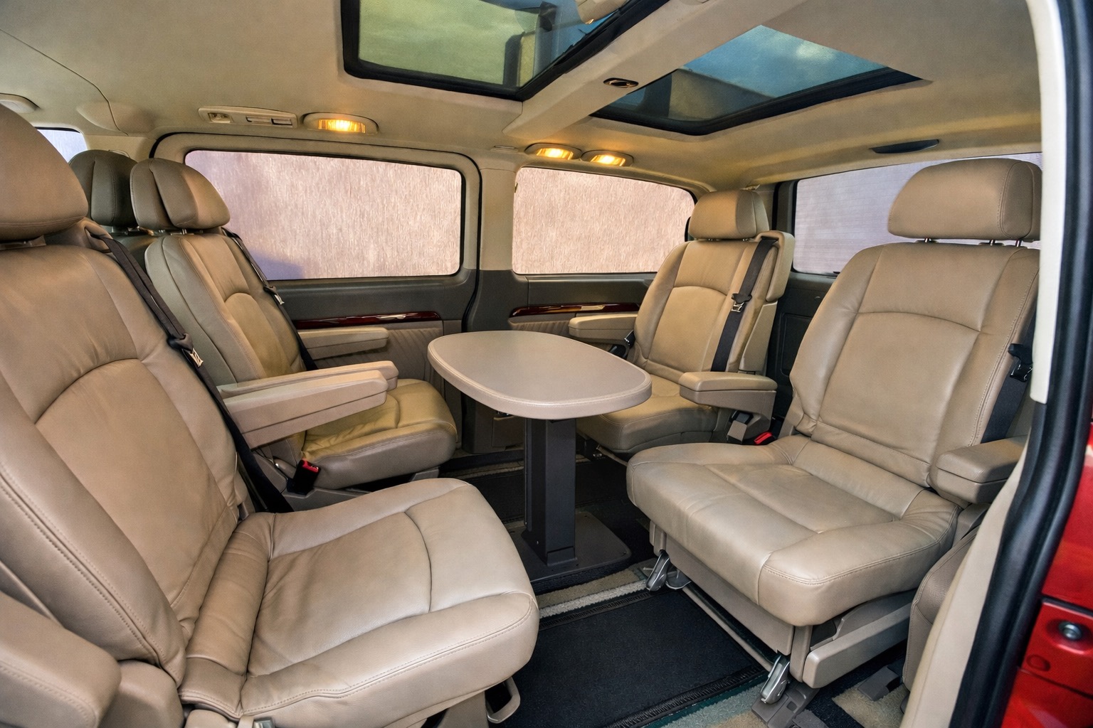 Luksusowe wnętrze busa z beżowymi skórzanymi fotelami i rozkładanym stolikiem, idealne do komfortowego przewozu osób w Łodzi. Widoczny szyberdach.