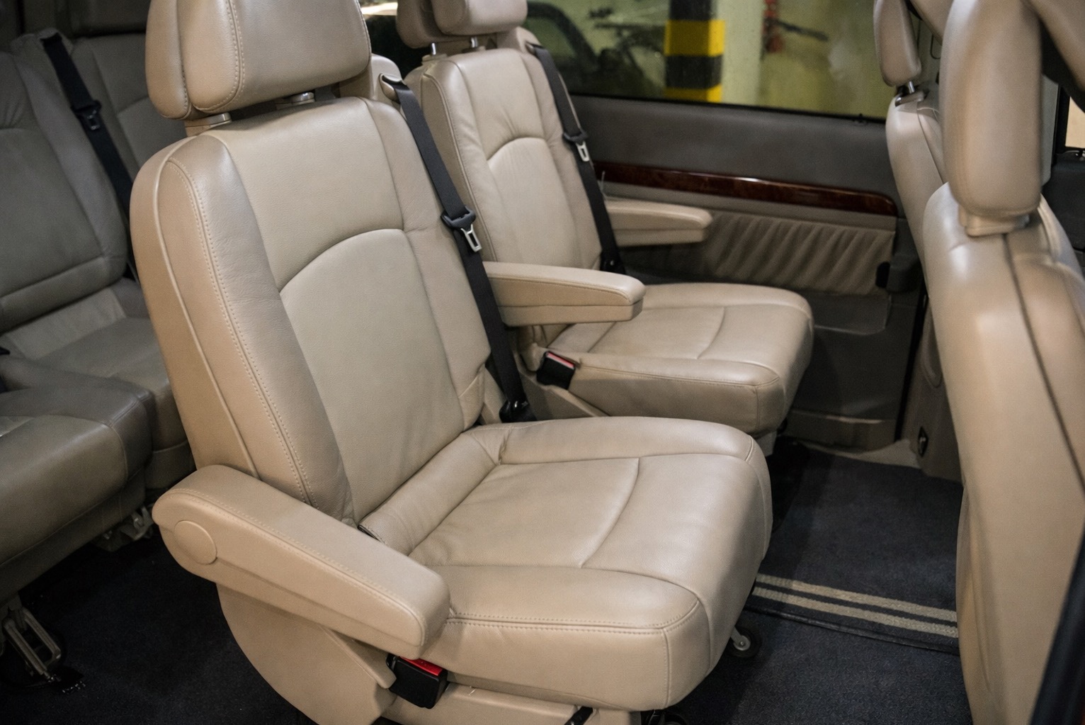 Wnętrze busa z beżowymi skórzanymi fotelami, widoczne pasy bezpieczeństwa i podłokietniki. Czyste i zadbane wnętrze pojazdu do przewozu osób.
