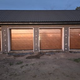 Portals - Dawid Bondos Okna Drzwi Bramy - Trzy brązowe bramy garażowe segmentowe z poziomym wzorem drewna, oddzielone szarymi słupkami z izolacją, w surowym stanie wykończenia budynku.