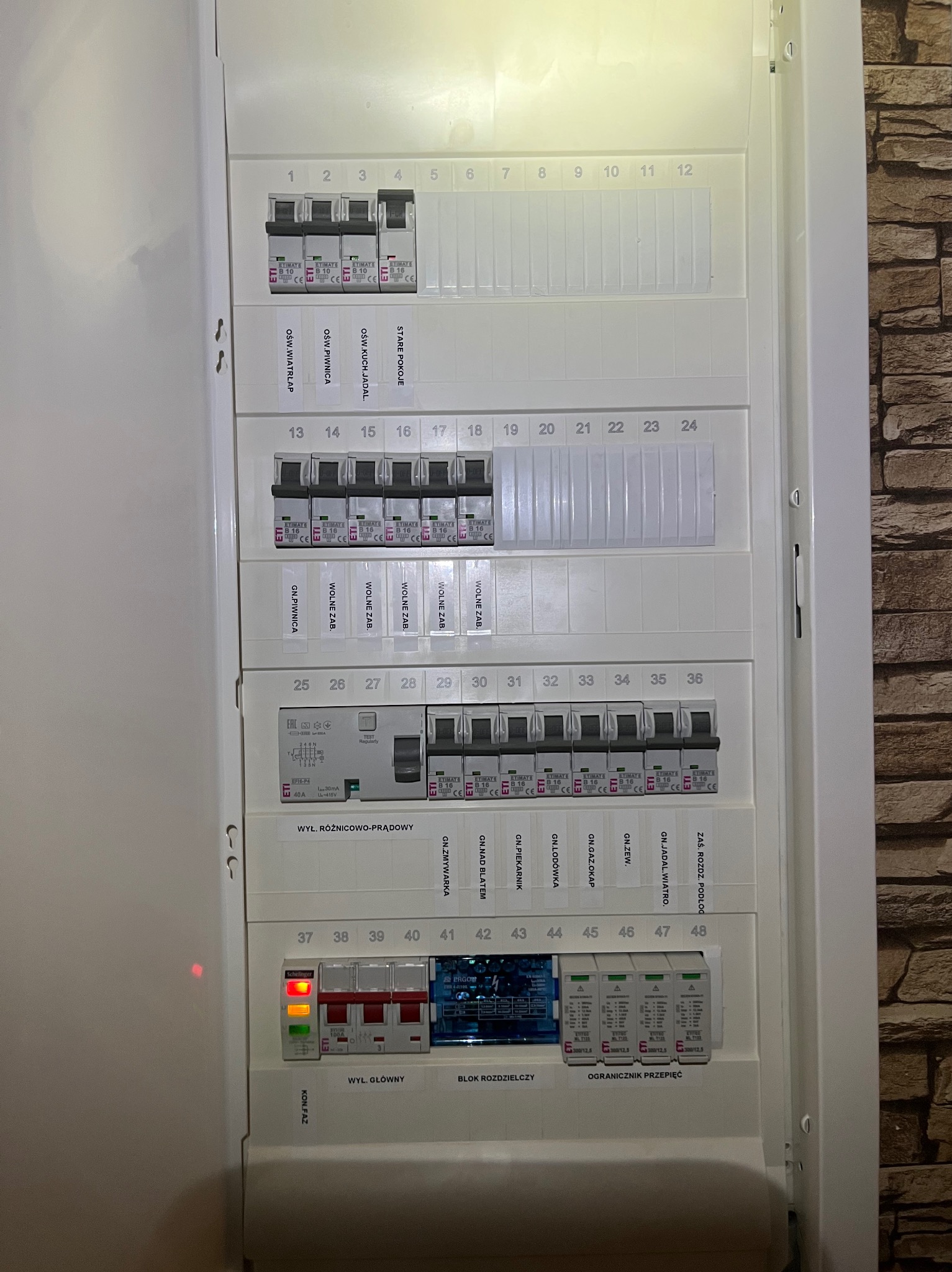 Rozdzielnica elektryczna z bezpiecznikami ETIMAT i wyłącznikiem różnicowoprądowym, widoczne oznaczenia obwodów i ograniczniki przepięć. Instalacja wewnątrz budynku.