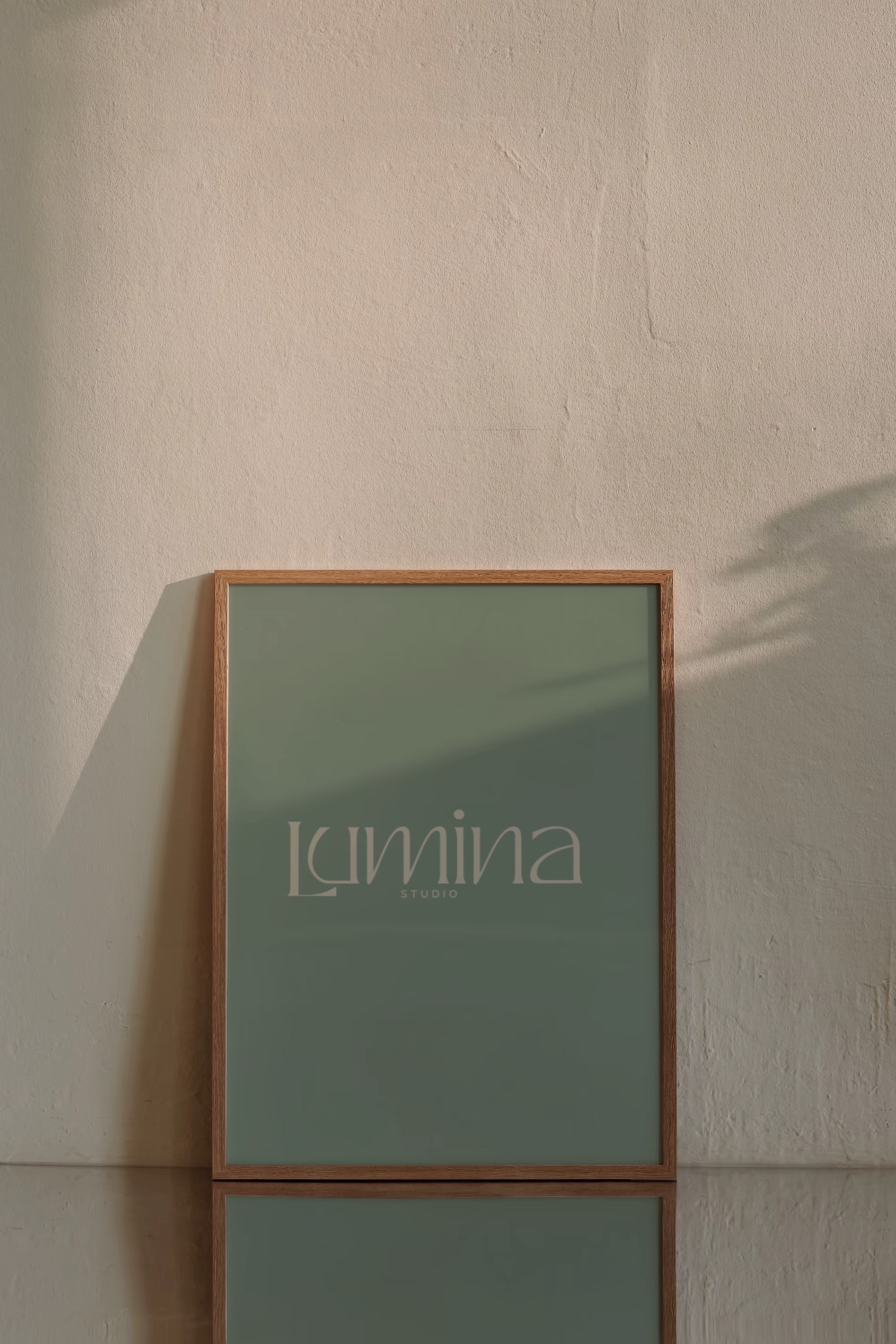 Oprawiony w drewno plakat z logo 'Lumina Studio' na tle beżowej ściany i lustrzanej powierzchni. Minimalistyczny design, stonowana kolorystyka, cień rzucany przez roślinę.