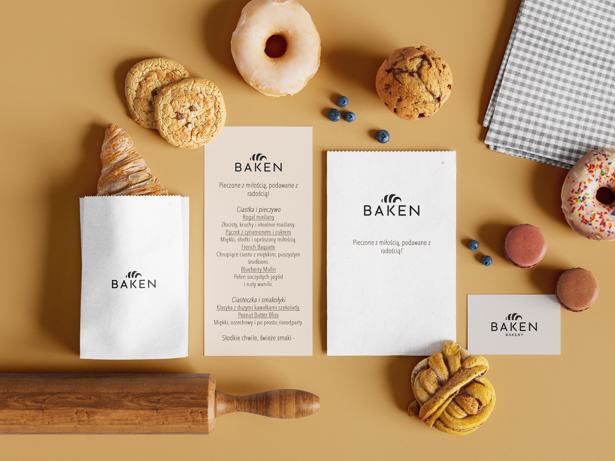 Kompozycja z pieczywem i ciastkami marki Baken Bakery na beżowym tle, z wałkiem do ciasta i ulotkami z opisem produktów. Widoczne detale i apetyczny wygląd.