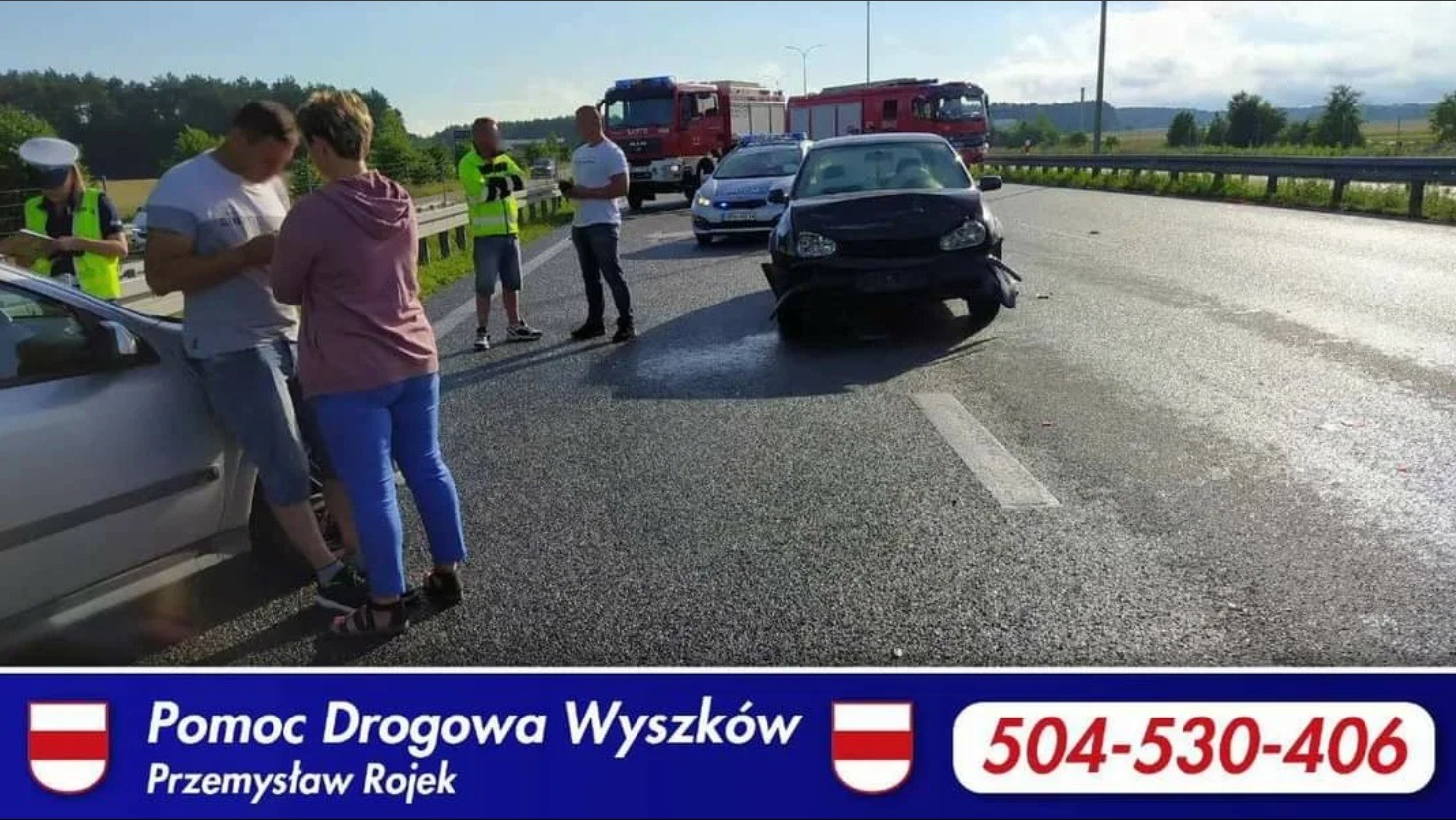 Uszkodzony samochód po kolizji na drodze, w tle wóz strażacki i policja. Na pierwszym planie osoby omawiające zdarzenie. Na dole baner z numerem telefonu.