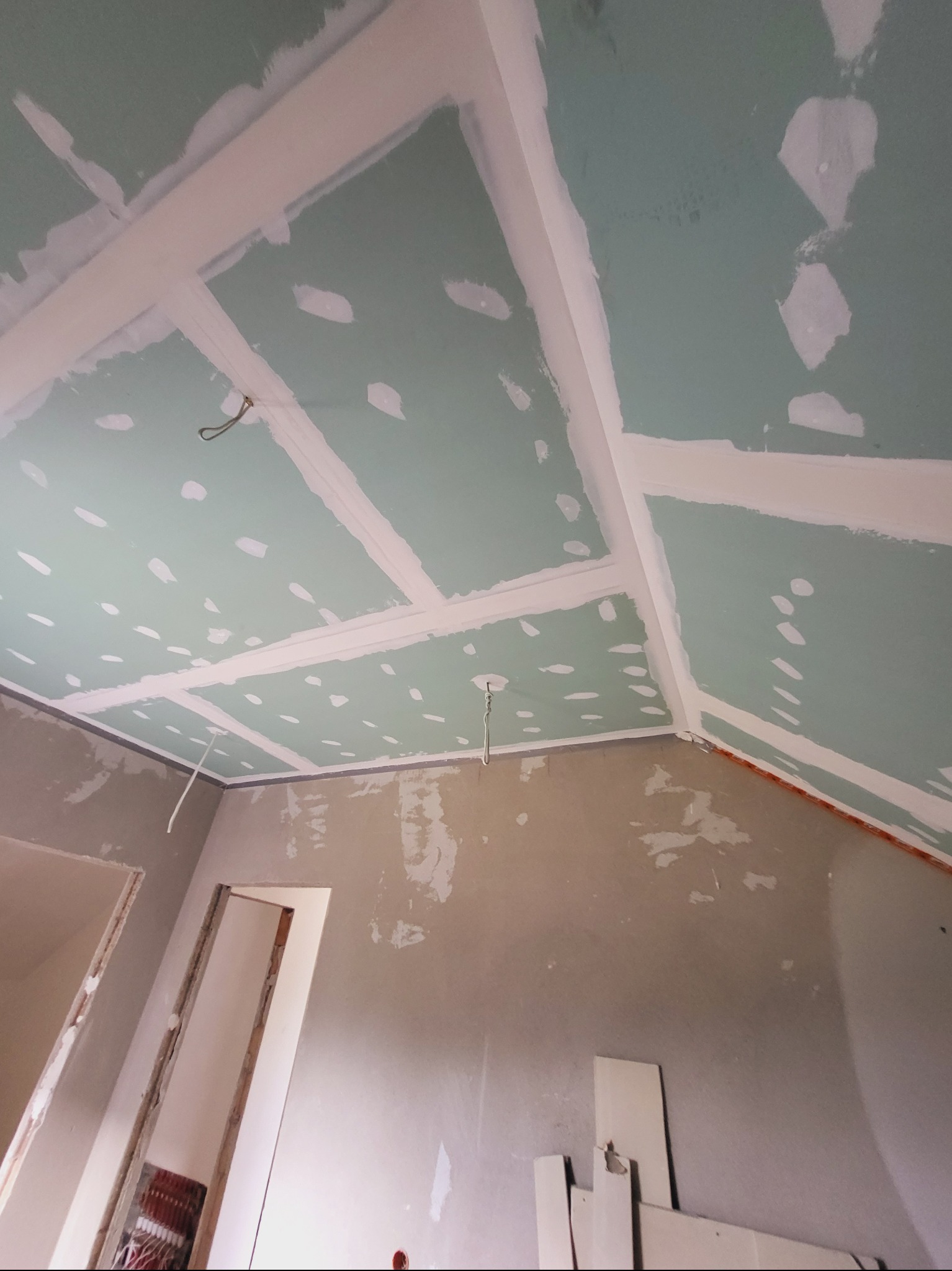 Skośny sufit z płyt kartonowo-gipsowych w trakcie szpachlowania, widoczne łączenia i ślady po wkrętach. W tle fragment ściany i ościeżnica drzwi.