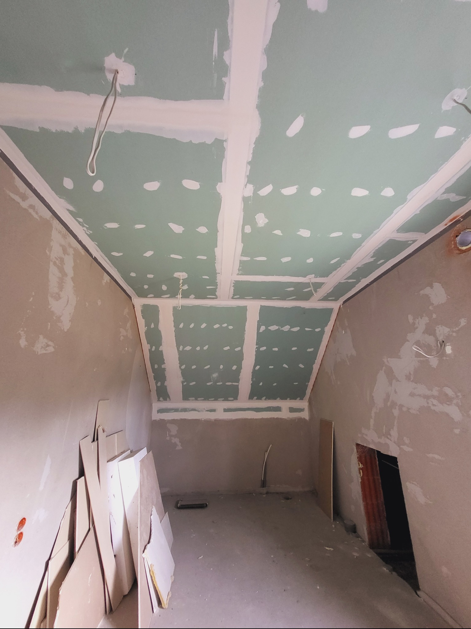 Sufit z płyt karton-gips, szpachlowane łączenia, widoczne kable, ściany w trakcie przygotowania do malowania. Prace wykończeniowe w pomieszczeniu ze skosami.