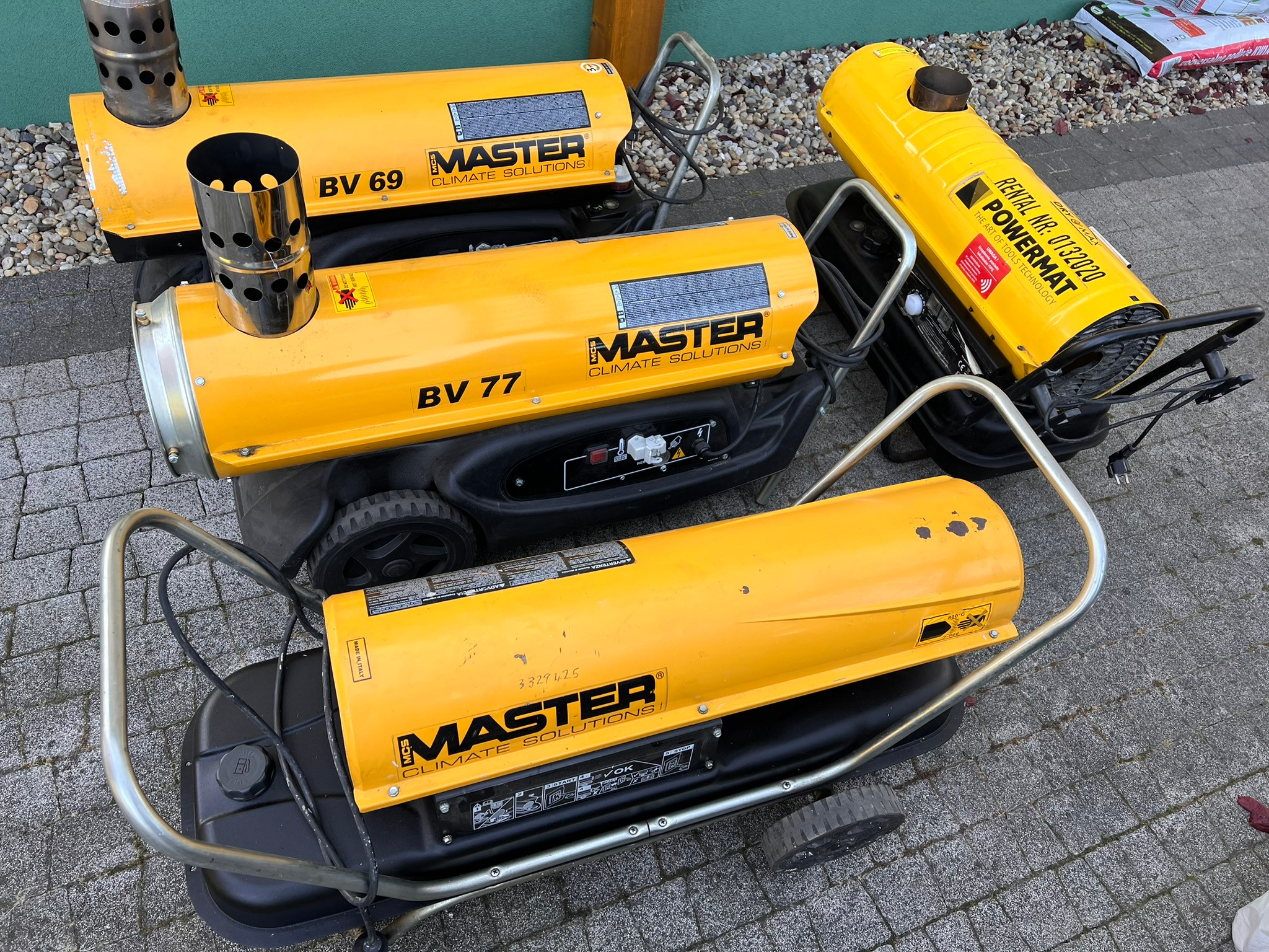Żółte nagrzewnice Master BV 69, BV 77 i Powermat na szarym bruku. Urządzenia z widocznymi oznaczeniami modelu i logo producenta, gotowe do użycia.
