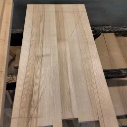 Paweł łuc - Deska z jasnego drewna z naniesionymi liniami cięcia, leżąca na warsztacie. Widoczne słoje drewna i precyzyjne oznaczenia. Przygotowanie do obróbki.