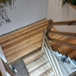 Paweł łuc - Jasne, drewniane schody z balustradą, widziane z góry. Na ścianach rośliny doniczkowe. Widoczne narzędzia na podeście. Nietypowy kąt ujęcia podkreśla naturalne drewno.