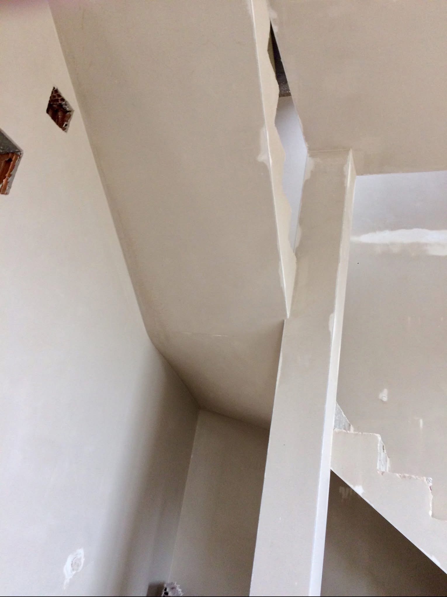 Gładkie, jasne ściany po nałożeniu tynku maszynowego, widoczne fragmenty schodów i filar. Świeżo otynkowane wnętrze w trakcie wykańczania.