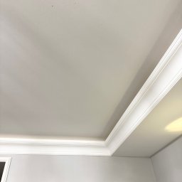 Walpol Waldemar Żochowski - Biały sufit z dekoracyjną listwą przysufitową, świeżo pomalowany na gładko, z widocznym fragmentem ściany w jasnym odcieniu szarości. Minimalistyczny design.