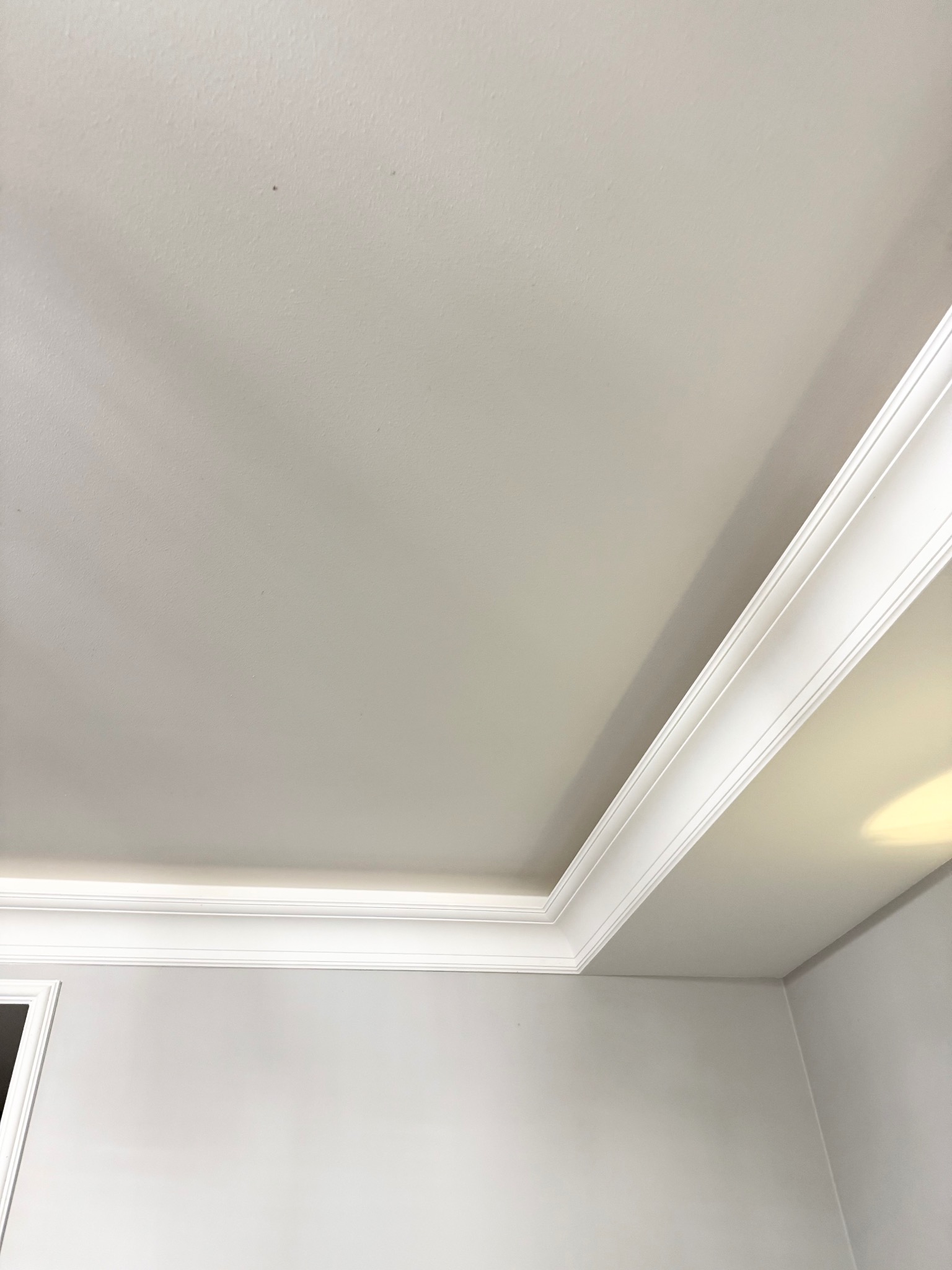 Biały sufit z dekoracyjną listwą przysufitową, świeżo pomalowany na gładko, z widocznym fragmentem ściany w jasnym odcieniu szarości. Minimalistyczny design.