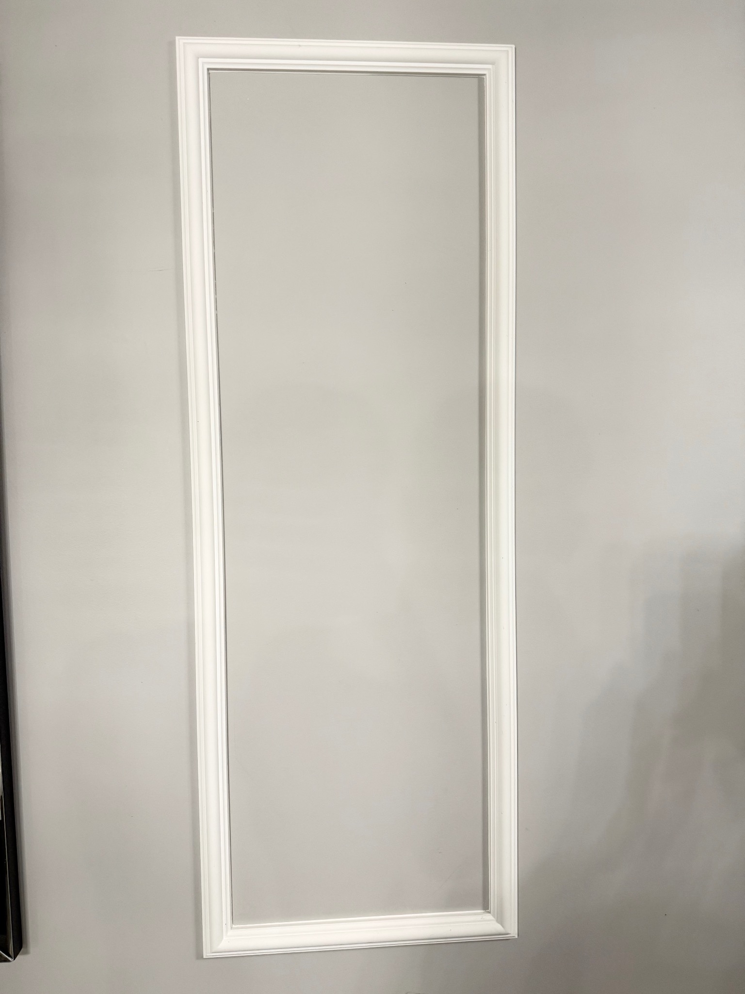 Biała, prostokątna listwa dekoracyjna na szarej ścianie, tworząca ramę. Minimalistyczny detal architektoniczny, podkreślający nowoczesny charakter wnętrza.