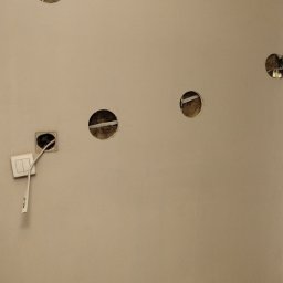 TOMASZ PIETRUCZANIS ELTECH SERWIS - Ściana z wywierconymi otworami pod punkty świetlne i gniazdko z wystającymi przewodami, w trakcie prac przygotowawczych do montażu oświetlenia.